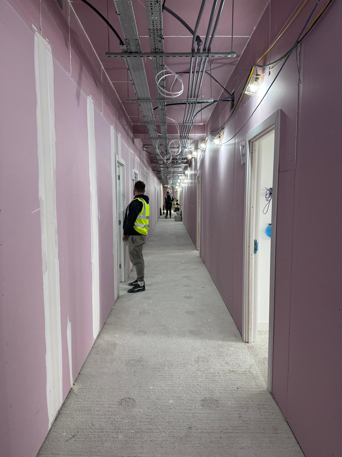Boarded corridor walls with taped joints and exposed overhead services