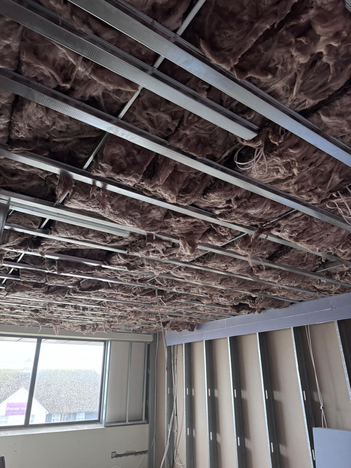 Insulation fitted above metal ceiling channels before boarding
